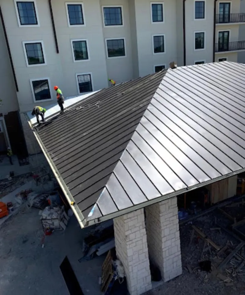 Crew installing standing seam metal roof panels on a commercial project in Macomb